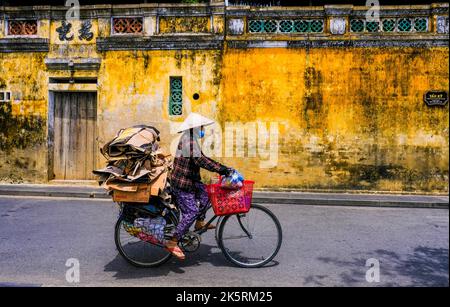 Una ciclista femminile corre in bicicletta lungo la strada nella città vecchia di Hoi An, Vietnam. Foto Stock