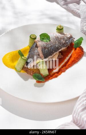 Piatto di pesce - Dorado con creme arcobaleno. Filetto di dorado con contorno, verdi e limone su piatto di ceramica su sfondo bianco per il menu del ristorante. Foto Stock