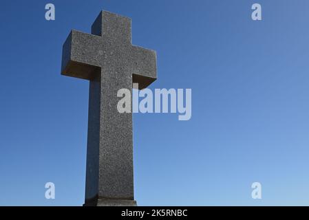 Croce di pietra funky, o crocifisso, con il cielo blu chiaro sullo sfondo Foto Stock