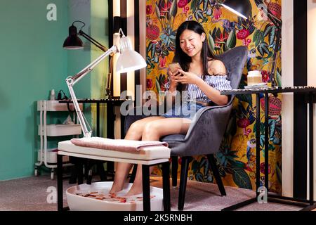donna che usa il telefono durante il trattamento pedicure Foto Stock