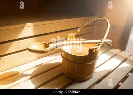 Secchio d'acqua con cucchiaio di legno per versare acqua su pietre calde nella sauna finlandese, spa e bagno termale a temperatura calda immagine concettuale. Foto Stock