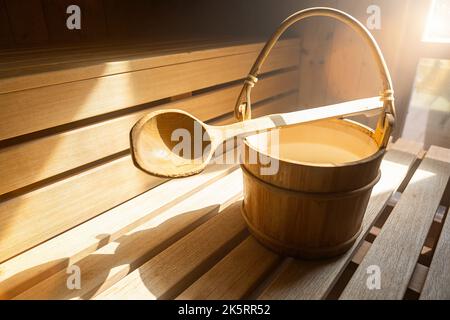 Cucchiaio in legno con secchio d'acqua per versare acqua su pietre calde nella sauna finlandese, spa e bagno termale a temperatura calda immagine concettuale. Sauna A. Foto Stock