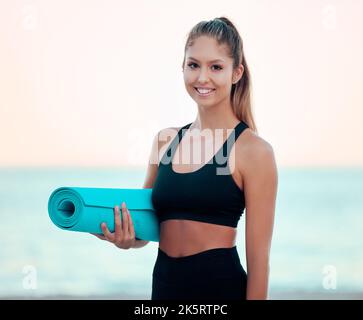 Bella donna che pratica yoga esercizio sulla spiaggia. Giovane donna che tiene il suo materassino yoga mentre sta fuori. Trovare pace interiore, equilibrio e. Foto Stock