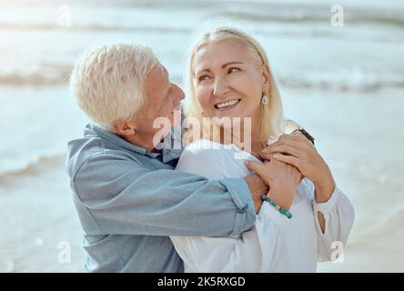 Una coppia caucasica matura felice godendo aria fresca in vacanza in spiaggia. Sorridente coppia in pensione abbracciando e abbracciando mentre si unisce all'esterno Foto Stock