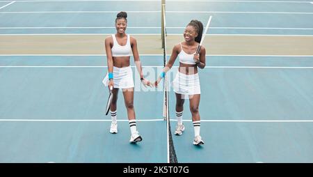 Giocatori di tennis che tengono le mani dopo una partita. Due donne che camminano in rete sul campo da tennis tenendo le mani. Giovani amici che si legano dopo il tennis Foto Stock