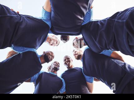 Sotto diversi gruppi di giocatori di rugby in piedi in un huddle insieme fuori su un campo. Giovani atleti maschi che guardano seri e concentrati mentre si sono accoccolati Foto Stock