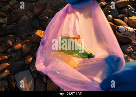 Pulizia dall'inquinamento ambientale. Un volontario che indossa guanti tiene una borsa aperta con rifiuti di plastica e bottiglie. Primo piano, vista dall'alto. Il concetto Foto Stock