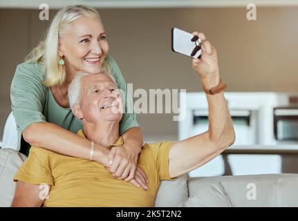 Coppia anziana felice che si unisce e che si gode la pensione insieme. Uomo e donna caucasici anziani affettuosi su un divano a casa mentre si prende Foto Stock