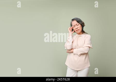 Stanco e stressato 60s anni donna asiatica in abiti casual toccando la fronte, gli occhi chiusi, che soffrono di emicrania o mal di testa, in piedi sopra l'isola Foto Stock