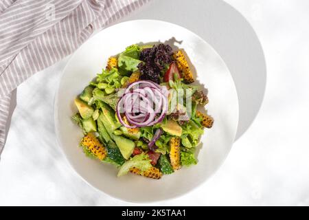 Insalata di cibo sano con verdure di edamame e avocado, fagioli di edamame, peperoni, mais, cetrioli, pomodori, cipolle rosse su fondo bianco per la res Foto Stock
