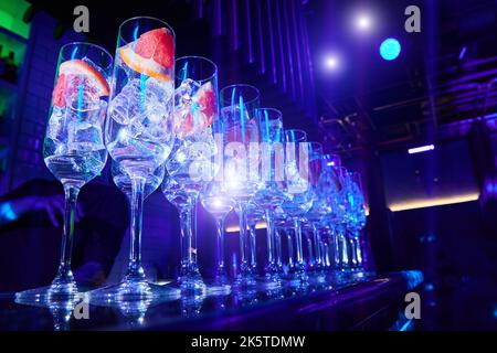 Una fila di bicchieri con fettine di pompelmo sul banco del bar nel processo di preparazione di cocktail alcolici Foto Stock