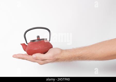 mano dell'uomo che tiene una teiera cinese rossa su uno sfondo bianco Foto Stock