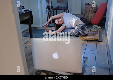 Una donna a casa che fa yoga e guarda una classe online. Foto Stock