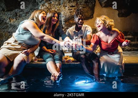 Un gruppo felice di giovani allegri multietnici che si divertono nella grotta termale del resort, che si rilassano facendo una festa insieme e brinicando facendo una bella festa Foto Stock