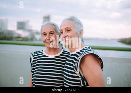 Ritratto di donne anziane felici, gemelli nello stesso vestito, a piedi sul ponte della città. Foto Stock