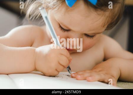 Primo piano ritratto di una adorabile bambina caucasica disegno con concentrazione utilizzando la penna nei taccuini del fratello. Sviluppo del bambino. Assistenza ai bambini. Foto Stock