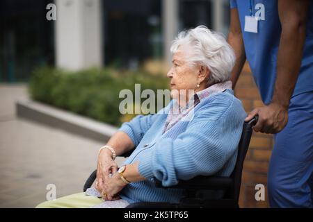 Ritratto di donna anziana in sedia a rotelle che trascorre il tempo all'esterno con la sua assistente. Foto Stock