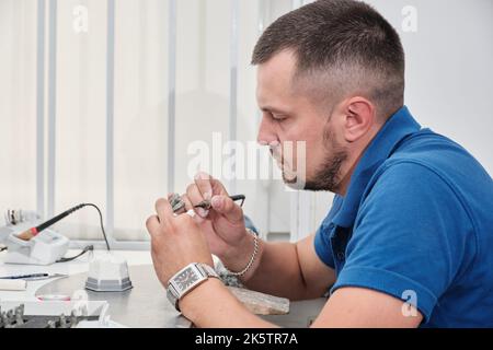 Dentista dentista uomo che lavora con dentiere nel suo laboratorio con cera. Tecnico dentale modellante corone di denti con cera calda. Foto Stock