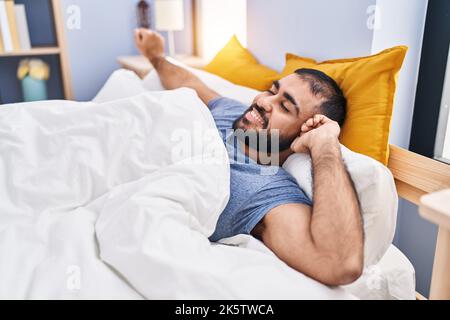 Giovane ispanico che si svegliò stendendo le braccia in camera da letto Foto Stock
