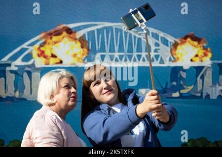 Kiev, Ucraina. 9th Ott 2022. Le donne prendono un selfie con un modello di francobollo che raffigura il ponte di Crimea in fiamme sullo sfondo, nel centro di Kyiv. Il 8 ottobre si verificò un'esplosione sul ponte di Crimea costruito in Russia che collegava la Russia e la penisola di Crimea da essa occupata, danneggiando parte della struttura del ponte. (Credit Image: © Oleksii Chumachenko/SOPA Images via ZUMA Press Wire) Foto Stock