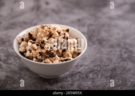 Il popcorn bruciato nel piccolo recipiente bianco su ceramica grigia Foto Stock