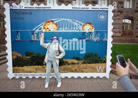 Kiev, Ucraina. 9th Ott 2022. Una ragazza si posa per una foto davanti a un mock-up di un francobollo raffigurante il ponte di Crimea in fiamme sullo sfondo, nel centro di Kyiv. Il 8 ottobre si verificò un'esplosione sul ponte di Crimea costruito in Russia che collegava la Russia e la penisola di Crimea da essa occupata, danneggiando parte della struttura del ponte. (Credit Image: © Oleksii Chumachenko/SOPA Images via ZUMA Press Wire) Foto Stock