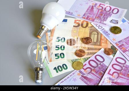 Spina elettrica, banconote in euro e centesimi con lampadina su sfondo grigio. Concetto per l'aumento del costo dell'elettricità. Energia costosa Foto Stock