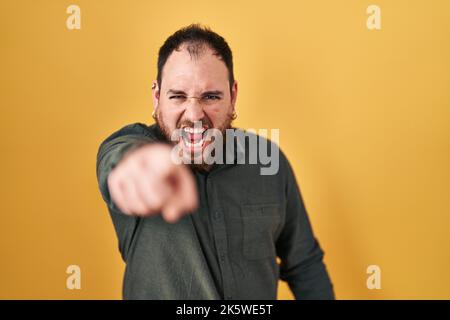 Più misura uomo ispanico con barba in piedi su sfondo giallo puntando dispiaciuto e frustrato alla macchina fotografica, arrabbiato e furioso con voi Foto Stock