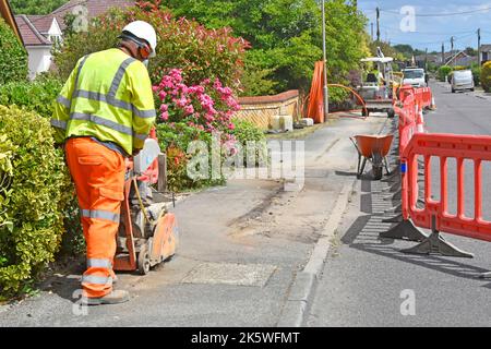Kit di salute e sicurezza indossato da lavoratori di cantieri stradali che utilizzano segatrice a disco nuovo sito sotterraneo di infrastruttura di cavi a banda larga Regno Unito Foto Stock