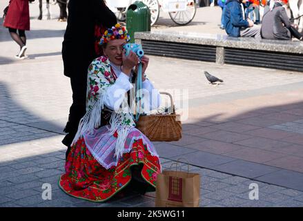 Cracovia, Malopolskie, Polonia - 24 marzo 2019: Una donna in costume nazionale polacco scatta una foto con una telecamera istantanea Fujifilm. Piazza principale del Foto Stock