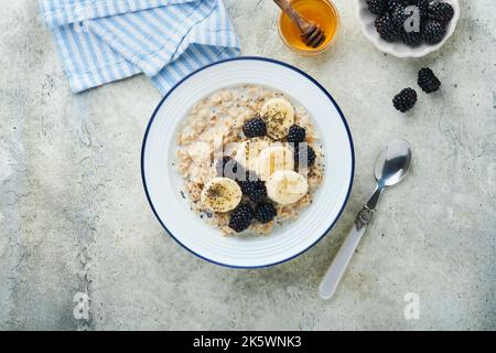 Farina d'avena. Ciotola di porridge di farinata d'avena con mora, banane e semi di chia su fondo grigio cemento vecchio tavolo. Vista dall'alto in stile piatto. Naturale i Foto Stock