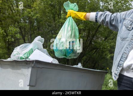Gettare spazzatura in un cestino. Primo piano di una mano che tiene un sacco di rifiuti sopra un cestino Foto Stock
