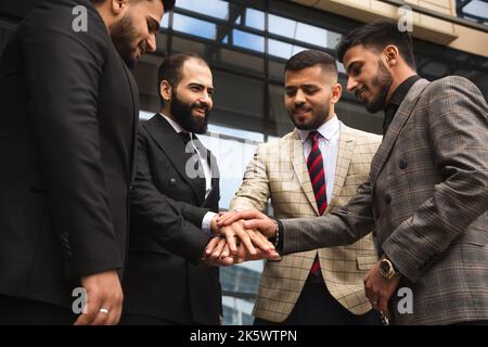 Team internazionale di imprese di persone di successo che celebrano la vittoria. Gli uomini in tute in una riunione aziendale gioiscono per i risultati della loro azienda Foto Stock
