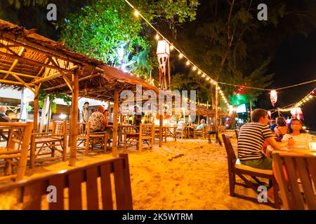 Koh Lanta, Thailandia - 10.11.2019: Vista di un piccolo bar sulla spiaggia di notte, sull'isola di Ko Lanta, Thailandia. Sedie e tavoli sono posti sulla sabbia. Molte lampadine Foto Stock