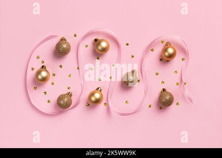 Cartolina di Natale con palline dorate, coriandoli a forma di cuore e nastro di raso su sfondo rosa Foto Stock