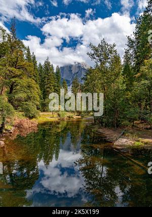 Le nuvole riempiono parzialmente un cielo blu sul fiume Merced, mentre El Capitan si affaccia in lontananza, il Parco Nazionale di Yosemite, California Foto Stock