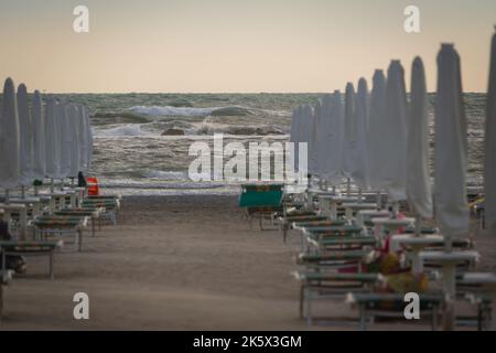 Le onde grandi si arrotolano sulla spiaggia. Vicino al parasol in giorno di sole luminoso. Bianco schiumoso onde e spruzzi. Una calda giornata estiva e alta onda, stagcape.Italy Foto Stock