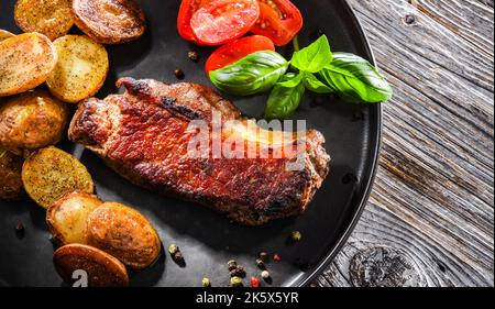 Bistecca di manzo fritta in padella con patate fritte e pomodori ciliegini. Foto Stock