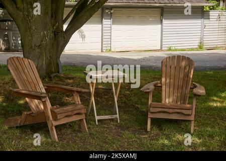 Due sedie in legno Adirondack vuote e tavolo pieghevole seduto all'ombra di un albero Foto Stock