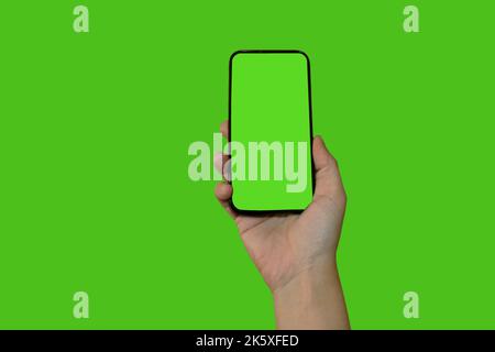 La mano di una donna tiene in mano uno smartphone con uno schermo verde. Oggetto isolato su sfondo verde. Modello per la progettazione. Mocap. Foto Stock