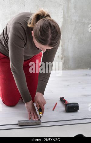 Il maestro femminile disegna una linea a matita sulla tavola, installando pavimenti in vinile al quarzo, lavori di installazione. Foto Stock