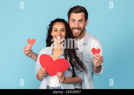 Ritratto di sorridente maschio caucasico millenario con barba e donna arabica che tiene il cuore Foto Stock