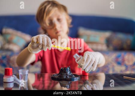 Ragazzo che fa esperimenti chimici a casa. Bambino con occhiali protettivi studia utilizzando la pipetta di gocciolamento di liquido in provetta, caucasico, biochimica Foto Stock