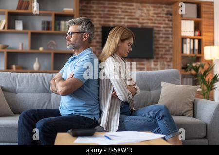 Offesa triste signora europea di mezza età ignora l'uomo dopo litigare sulle fatture nel soggiorno interno Foto Stock