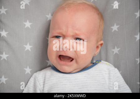 Ritratto del neonato piangente, primo piano. Tagliare il bambino con gli occhi blu. Espressione del volto. Foto Stock