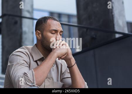 Primo piano ritratto foto di sconvolto lavoratore di ufficio licenziato uomo d'affari in depressione, uomo con gli occhi chiusi seduto sulle scale di ufficio edificio fuori. Foto Stock