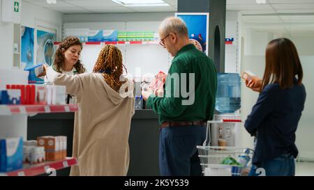 Farmacista femminile che serve clienti con pillole e farmaci, scansione di prodotti medicinali e assistenza in farmacia. Operaio medico che aiuta le persone ad acquistare cure e farmaci. Foto Stock