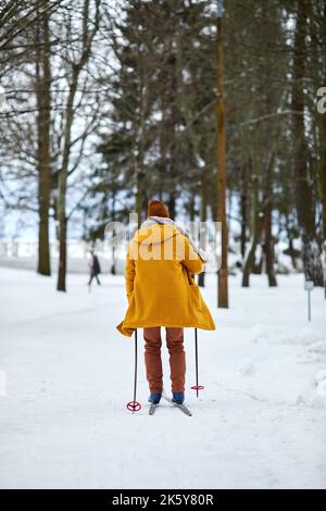 Vista sul retro del giovane sciare nella foresta invernale mentre vi godete attività all'aperto Foto Stock