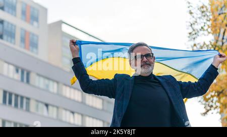 Orgoglioso cittadino ucraino protestare pacificamente contro la violenza russa camminando per la strada e tenendo la bandiera blu-e-gialla dietro di lui. Inquadratura media all'aperto. Foto di alta qualità Foto Stock