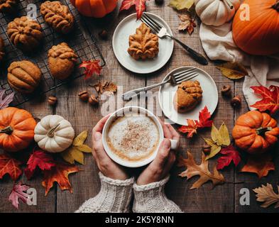 Vista dall'alto delle torte di spezie di zucca a forma autunnale e del latte che tiene le mani. Foto Stock